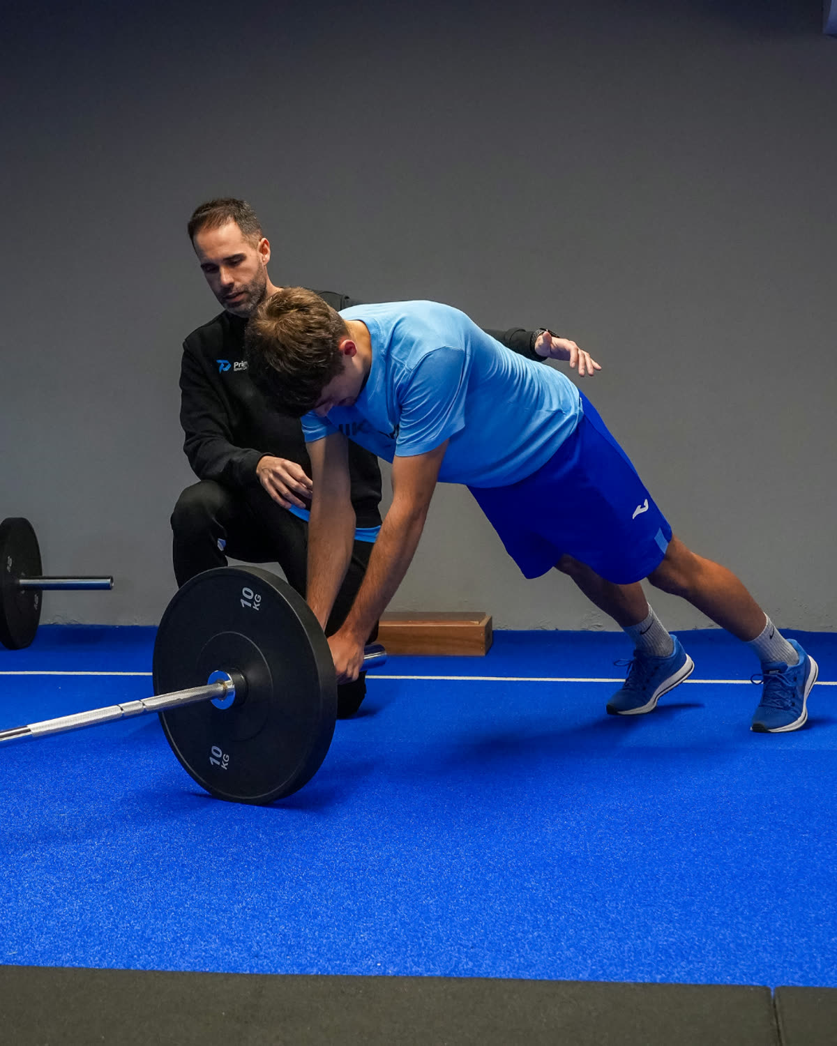 Entrenador de Prime Sport Center corrigiendo la técnica de peso muerto de un joven futbolista