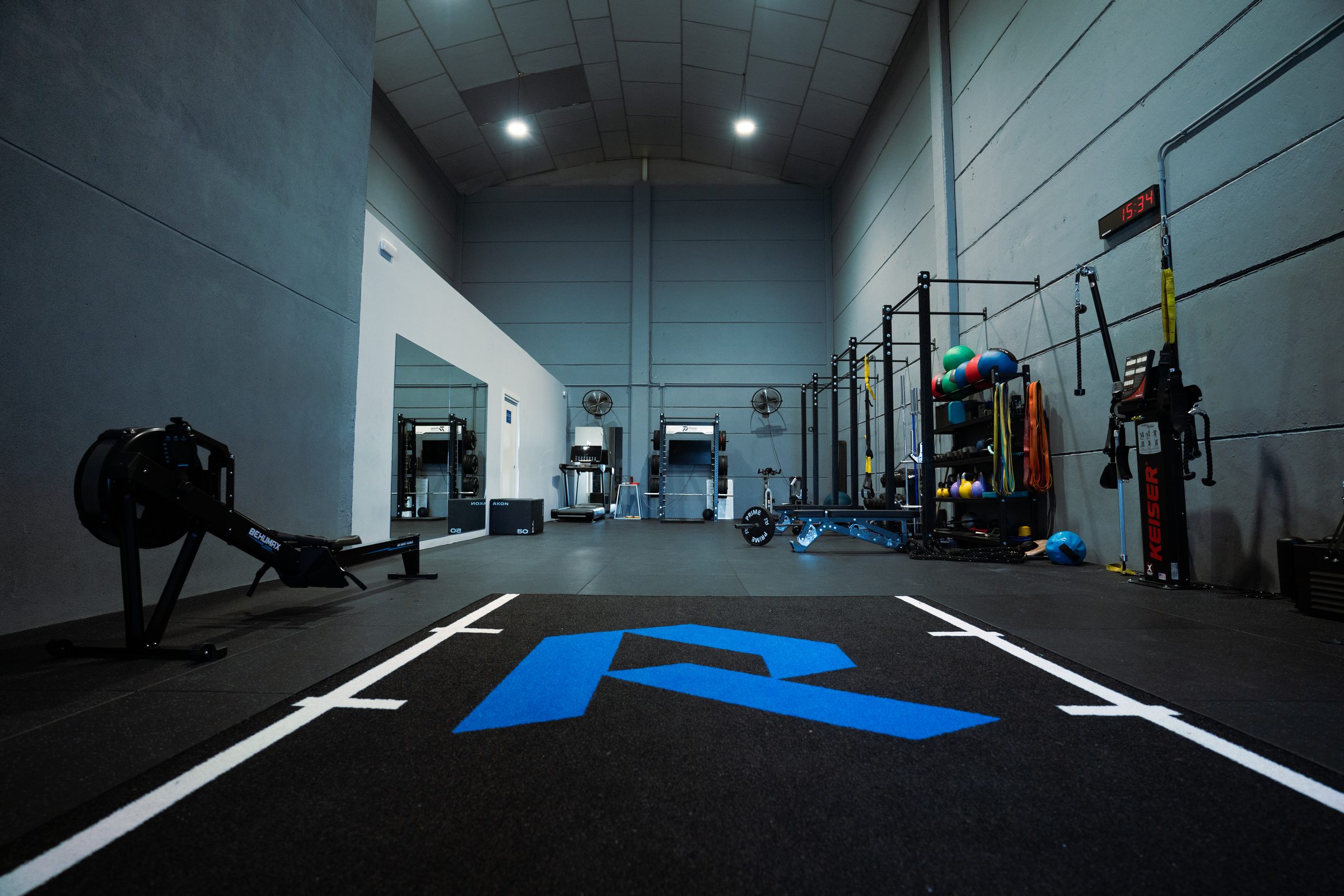 Sala de entrenamiento de Prime Sport Center con el logotipo azul en el suelo y material de fuerza y readaptación